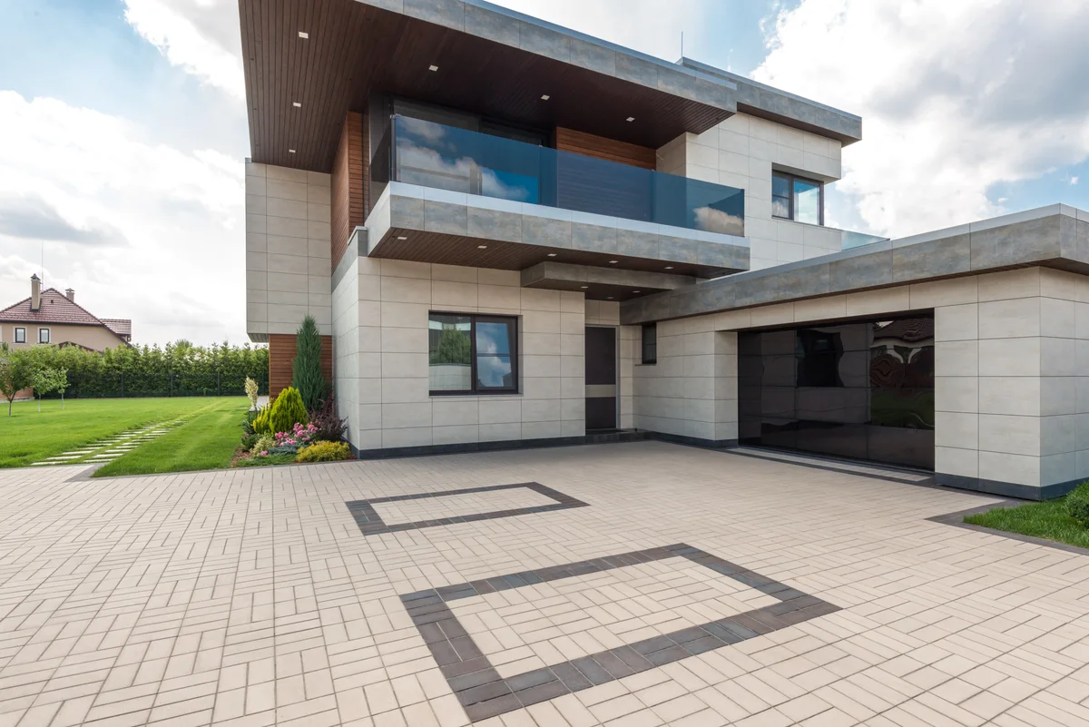 A wide paver driveway with a dark inlaid border running up to a modern house