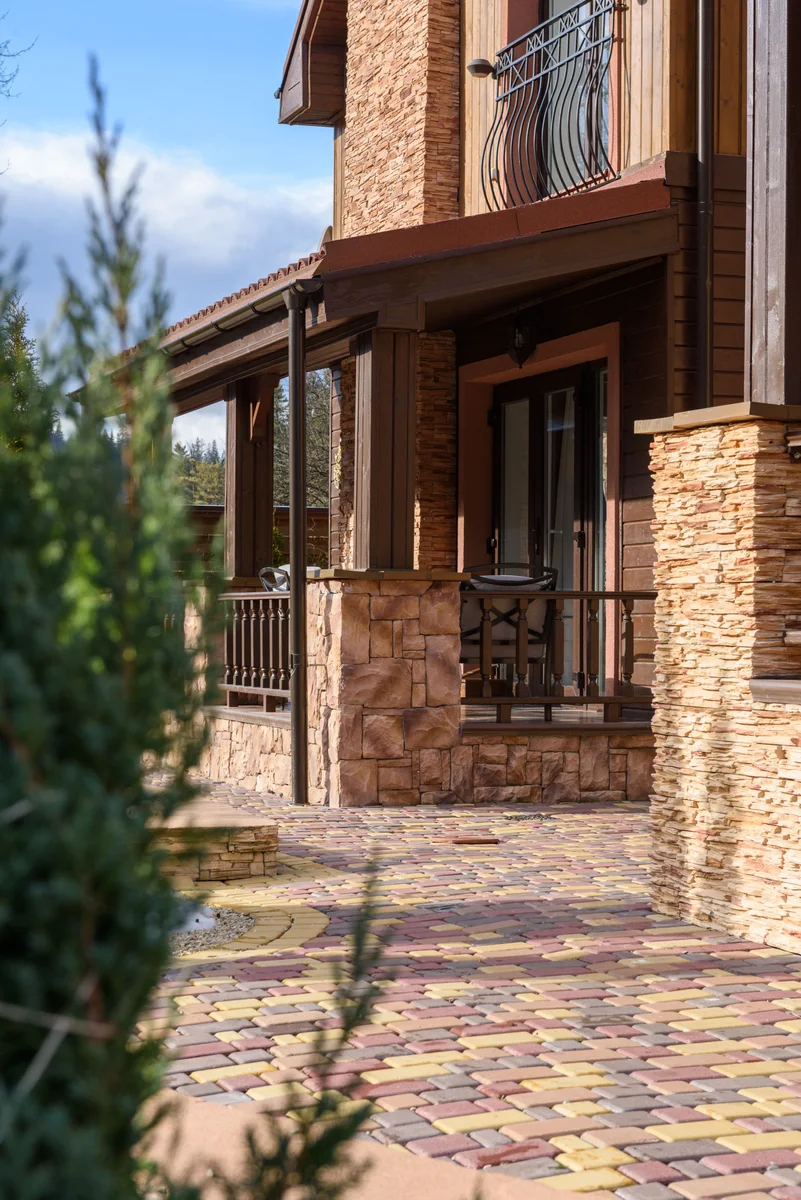 A covered porch with a stone clad pier and mixed colour pavers running up to it
