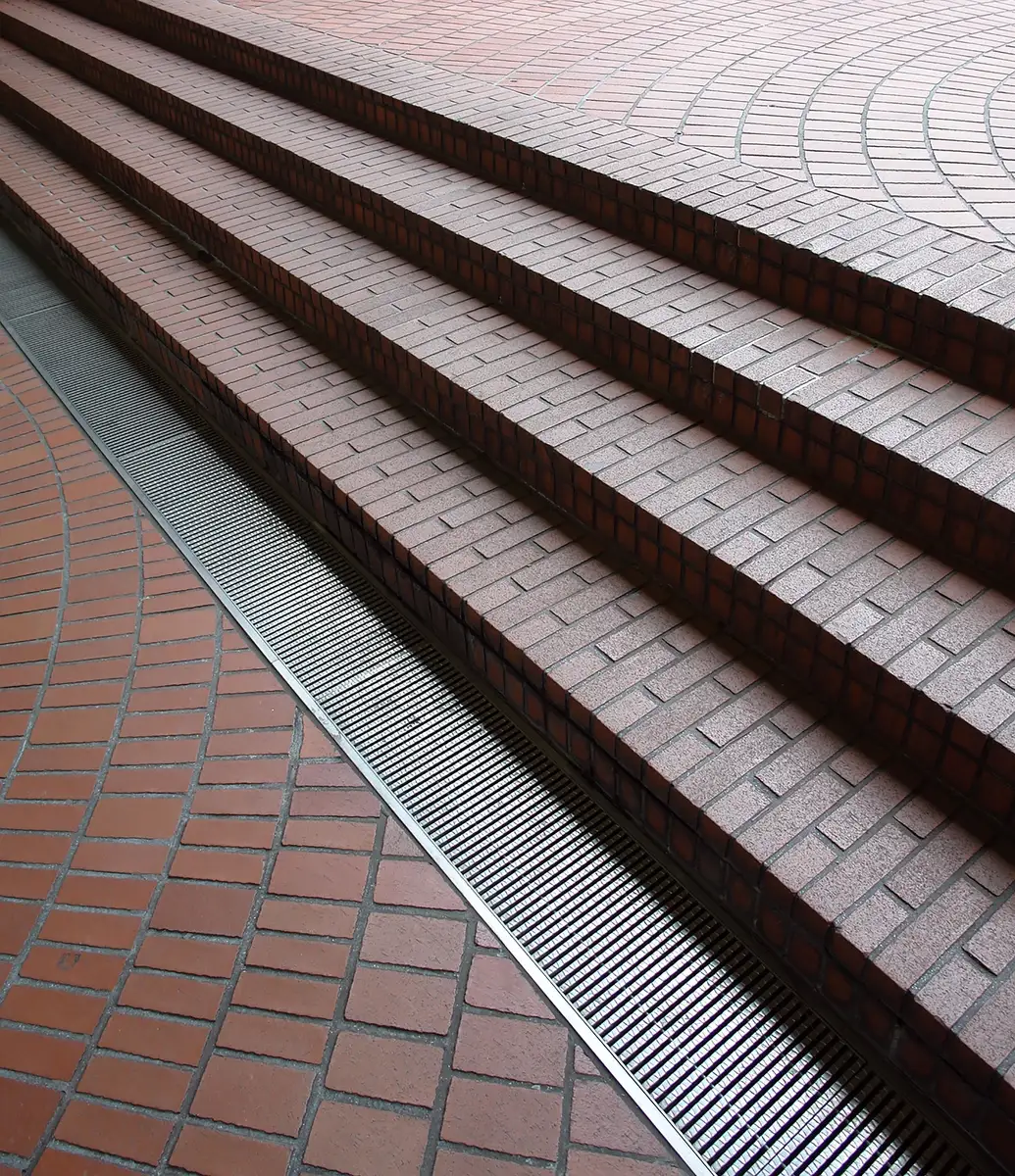 A linear channel drain running along the foot of brick steps